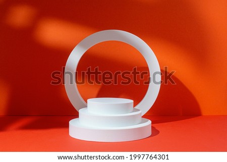 White circle and oval podiums for presentation under tropical leaves on a red background. 