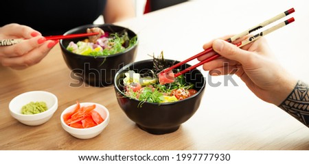 Man and woman eating poke salad with chopsticks. Dab tuna salad in a bowl. People in the restaurant eat salad with chopsticks. Asian seafood salad concept
