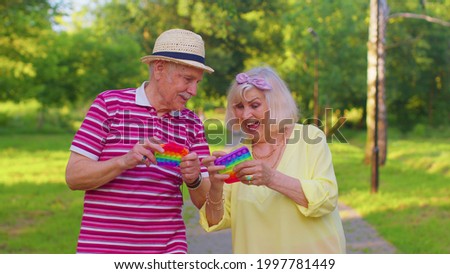 Senior stylish couple grandmother grandfather squeezing presses colorful anti-stress push pop it popular toy in park. Old mature family play trendy fidgeting sensory game with buttons. Stress reliever Royalty-Free Stock Photo #1997781449