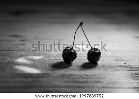 Ripe red cherries lie on the table in the rays of light on a dark background. Black and white photo