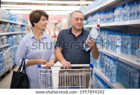 Mature family of retirees considering bottle of drinking water in department of supermarket
