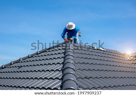 Roofer at work, installing clay roof tiles,Construction roofer installing roof tiles at house building site Royalty-Free Stock Photo #1997909237