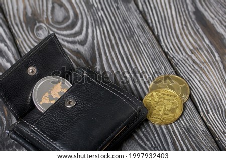Cryptocurrency coin in an open wallet. Nearby are coins of other cryptocurrencies. On brushed pine boards.