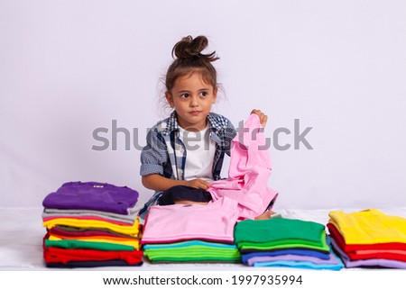 A boy wearing a plaid shirt holding a pink shirt swinging in a pile of colorful shirts 
in a white background.The concept of independent play of the child.
