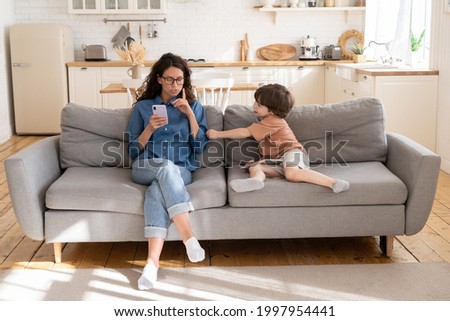 Young mom or babysitter use smartphone ask little kid to be quit and calm. Bored child disturb mother from work in mobile phone, message reading or shopping online. Preschool son need mum attention