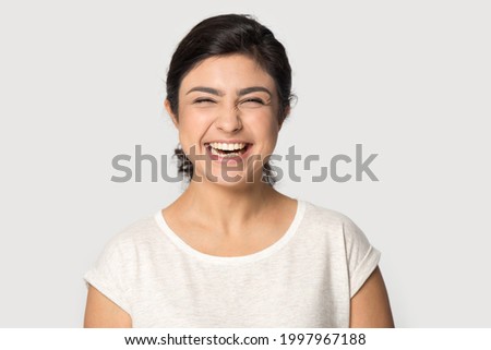 Profile picture of overjoyed millennial Indian female isolated on grey studio background laugh at funny joke. Headshot portrait of happy excited young mixed race woman smiling. Humor, fun concept.