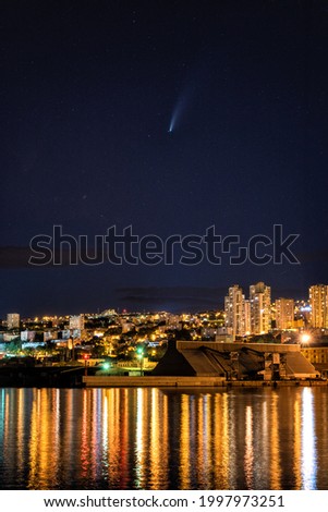 Comet Neowise over Rijeka port city on Adriatic sea, Croatia. Amazing night cityscape with city lights, blue starry sky and reflection in the water, outdoor travel and scientific background