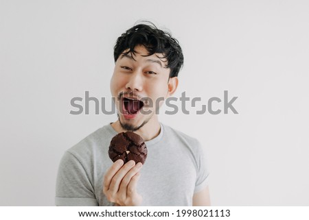 Funny face Asian man eat chocolate cookie isolated on white background. Royalty-Free Stock Photo #1998021113