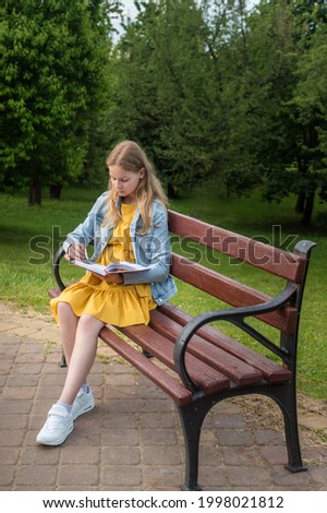 teenage girl reads a book on a bench in the summer park. Vertical photo