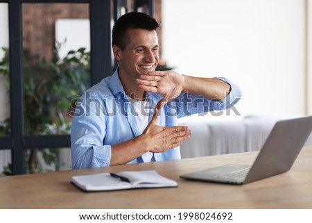 Happy smiling deaf young caucasian man uses sign language while video call using laptop while sitting at home, virtual communication concept