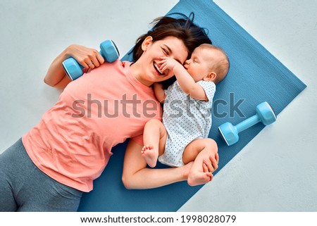 A sports mother is engaged with the child in fitness and yoga at home. The concept of sports, motherhood and an active lifestyle. Young woman in sports training with her child. Royalty-Free Stock Photo #1998028079