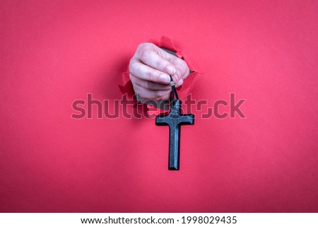 Wooden cross with a leather cord in a woman's hand on a red paper background.