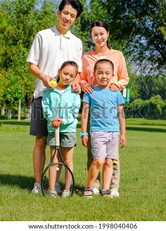 Happy family of four playing tennis in the park high quality photo