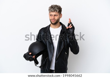 Young man with a motorcycle helmet isolated on white background with fingers crossing and wishing the best