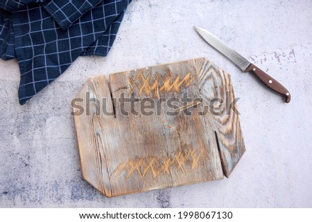 Empty wooden cutting board, knife and checkered navy blue towel on kitchen table background. 