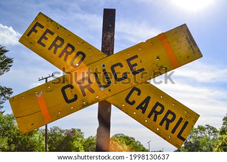 Cross-shaped yellow sign that reads in Spanish "Cruce Ferrocarril". Careful driving, transportation warning. Railway crossing, daylight. Tacuarembó, Uruguay