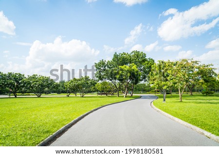 Beautiful green city park with blue sky. Pathway and beautiful trees track for running or walking and cycling relax in the park on green grass field on the side. Sunlight and flare background concept. Royalty-Free Stock Photo #1998180581