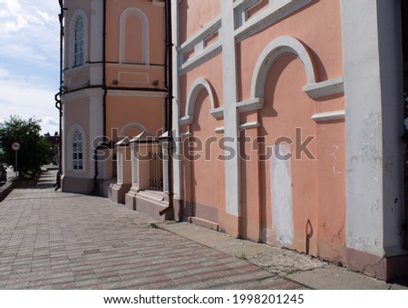 the street is paved with cobblestones, a historic peach-colored building with white trim. a sunny summer day