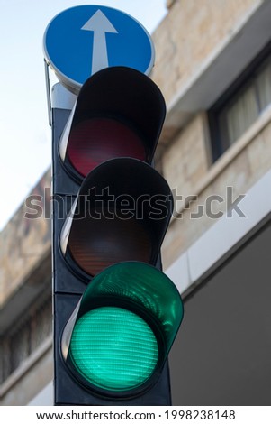 Green color on the traffic light lens In city With straight forward arrow sign above, blue sky background . Close-Up Of Road Signs on the street. Blue arrow sign while sunset.
