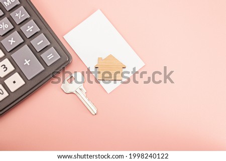 The concept of mortgage, sale and rental of housing and real estate. Mortgage credit lending. Calculator with a wooden house and a key on a delicate pink background. Copy space. Mock-up