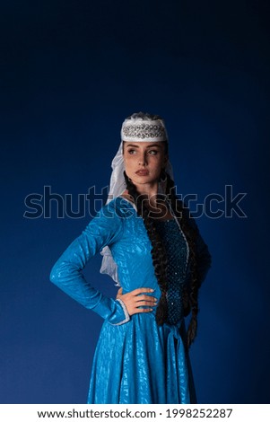Beautiful girl with black tresses in traditional Georgian dress on dark blue background. High quality picture of authentic Caucasian dancers performing on dark blue matte background