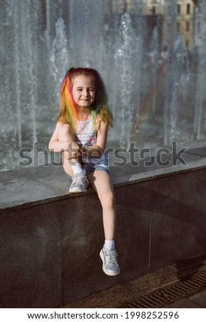 portrait of cute caucasian smiling girl with colorful dyed hair sitting in front of splashing fountain. Image with selective focus