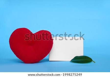 Mock up. A stuffed toy heart and a ficus leaf on a solid blue background. Copy space