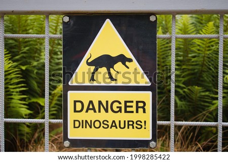 Warning sign, danger dinosaurs, on metal fence with foliage in the background, close up