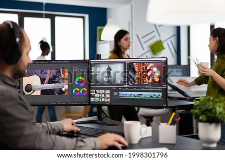 Creator content wearing headphones editing film montage in post production software at computer with dual monitors setup. Videographer cutting and prosessing movie footage in creative agency office