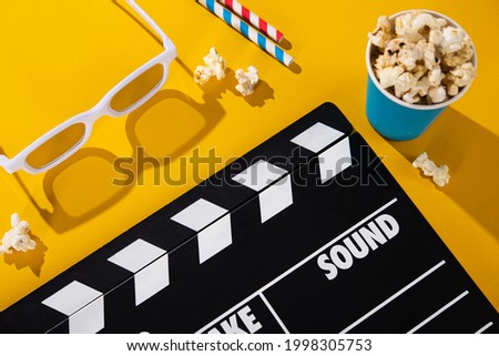 3D glasses, popcorn in a box, clapper board, colored cocktail tube on a yellow background. cinema cocncept. Top view