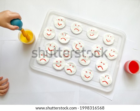 The study of emotional intelligence. Children's emotions. Children's hands with yellow and red emoticons. Montessori concept. The child draws with paints. Fine motor skills. Children's experiences. Royalty-Free Stock Photo #1998316568