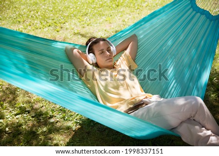 Audio healing. woman in headphones listens to audio recordings from the phone  lie in a hammock in a summer park or garden.