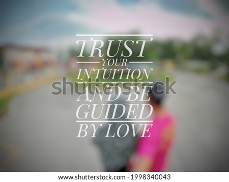 Inspirational love quote "TRUST YOUR INTUITION AND BE GUIDED BY LOVE" isolated on a blurry background.
