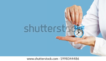 Doctors hands holding blue alarm clock over blue background. Time is crucial life saver. Medical banner. Copy space. Book appointment or checkup time reminder. Schedule. Opening hours deadline