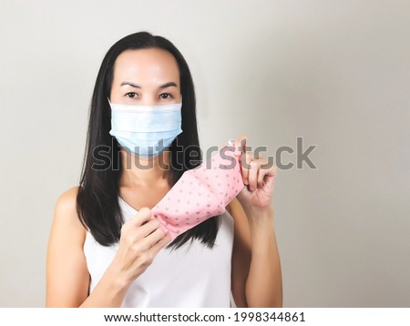Portrait of Asian woman wearing surgical  face mask holding pink polka dot cloth face mask to put on for better protection from covid-19 outbreak - concept of safety, healthcare, medical and hygiene.