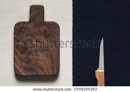 Hand-made small black walnut wooden chopping board and a knife on the numb. Two-color linen combination texture background.