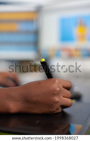 Close up of african photo retoucher holding stylus pen editing customer photo using computer with two displays. Black woman editor retouching assets drawing on graphic tablet in creative agency office