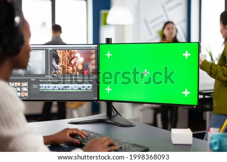 African video editor with headset editing footage using pc with greenscreen, chroma key isolated display sitting in creative agency. Videographer in digital multimedia company processing movie