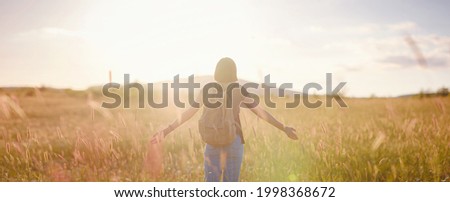 Trendy young woman with a backpack in a field at sunset. Freedom and nature concept. Soft focus