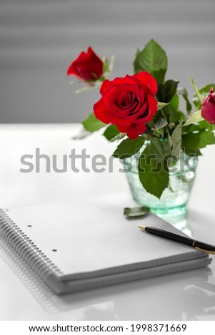 A bouquet of red roses in a glass transparent vase. Notebook and pen. Place for your text. Copy space. High quality photo
