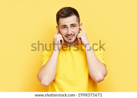 Handsome funny man covering his ears with hands afraid to hear bad news isolated on yellow background. silence concept