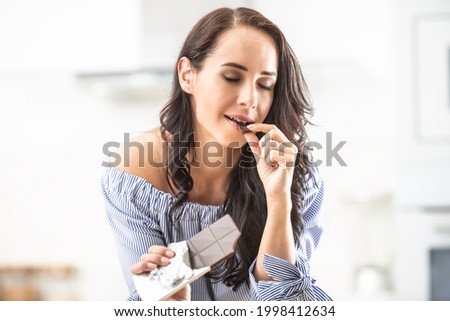Indulgence of chocolate by a woman indoors biting from it with eyes closed. Royalty-Free Stock Photo #1998412634