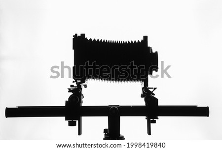 Silhouette of old bellows camera on tripod, horizontal white background, with copy space