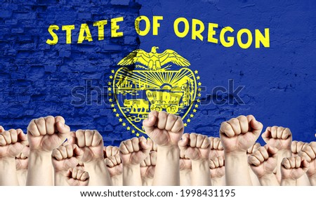 Raised fists of men against the background of the flag of State of Oregon painted on the wall, the concept of popular unity and the opinion of the majority.