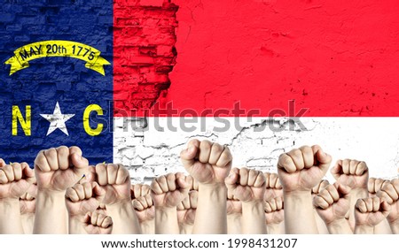 Raised fists of men against the background of the flag of State of North Carolina painted on the wall, the concept of popular unity and the opinion of the majority.