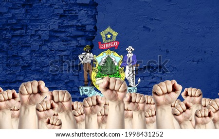 Raised fists of men against the background of the flag of State of Maine painted on the wall, the concept of popular unity and the opinion of the majority.