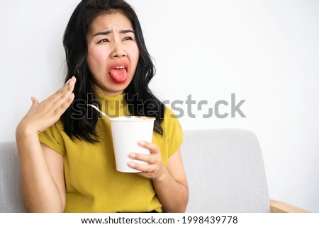Asian woman eating very hot and spicy noodle from a cup her mouth and tongue burning and red  Royalty-Free Stock Photo #1998439778