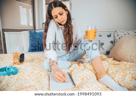 Angry woman talking on a cellphone while drinking juice in her bed.
