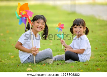 Two cute little girl asia playing on the colorful toy windmill  in her hands at the lawn. Which increases the development and enhances learning skills renewable energies and sustainable resources.