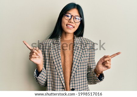 Young chinese woman wearing business style and glasses smiling confident pointing with fingers to different directions. copy space for advertisement 